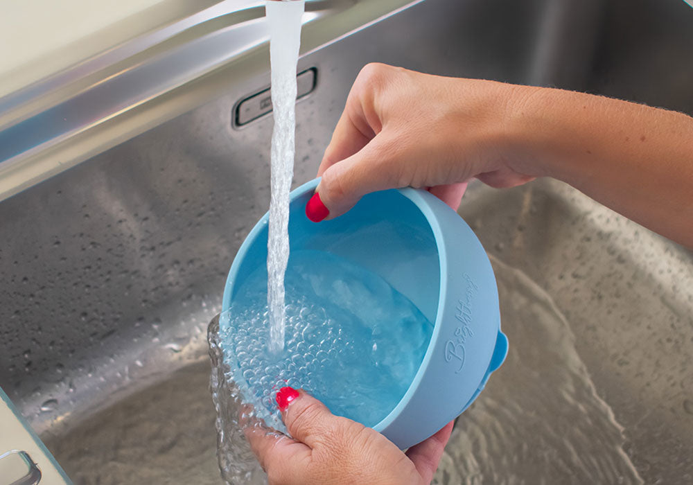 women's hands washing Brightberry silicone suction bowl under clean tap water